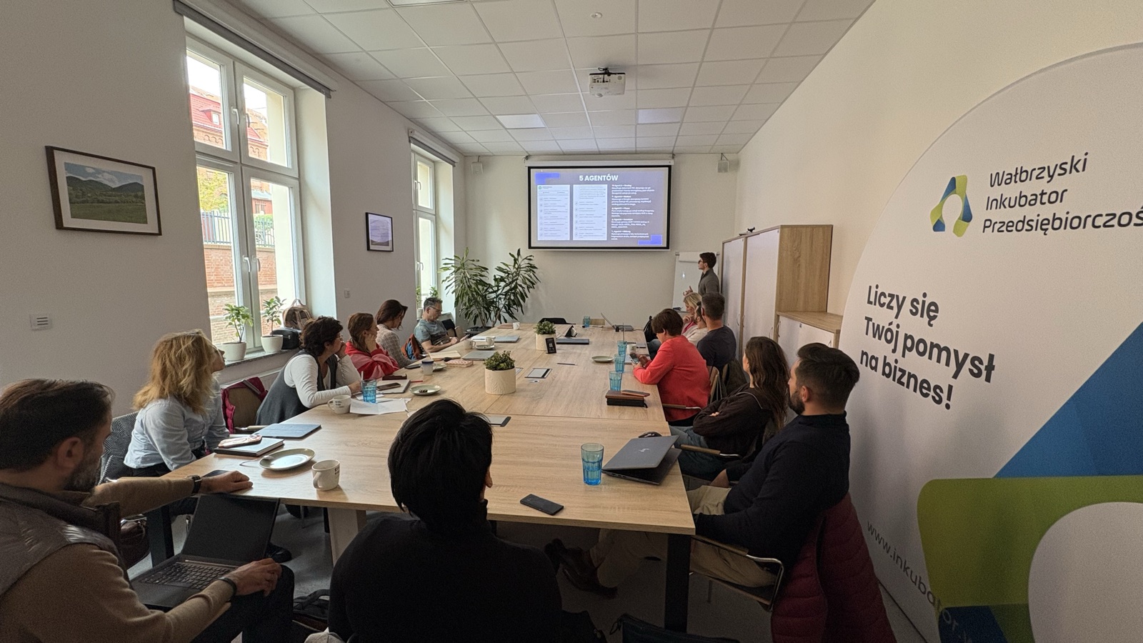 About fifteen people around a long table at the Wałbrzych Business Incubator, watching a slide titled 5 agentów.