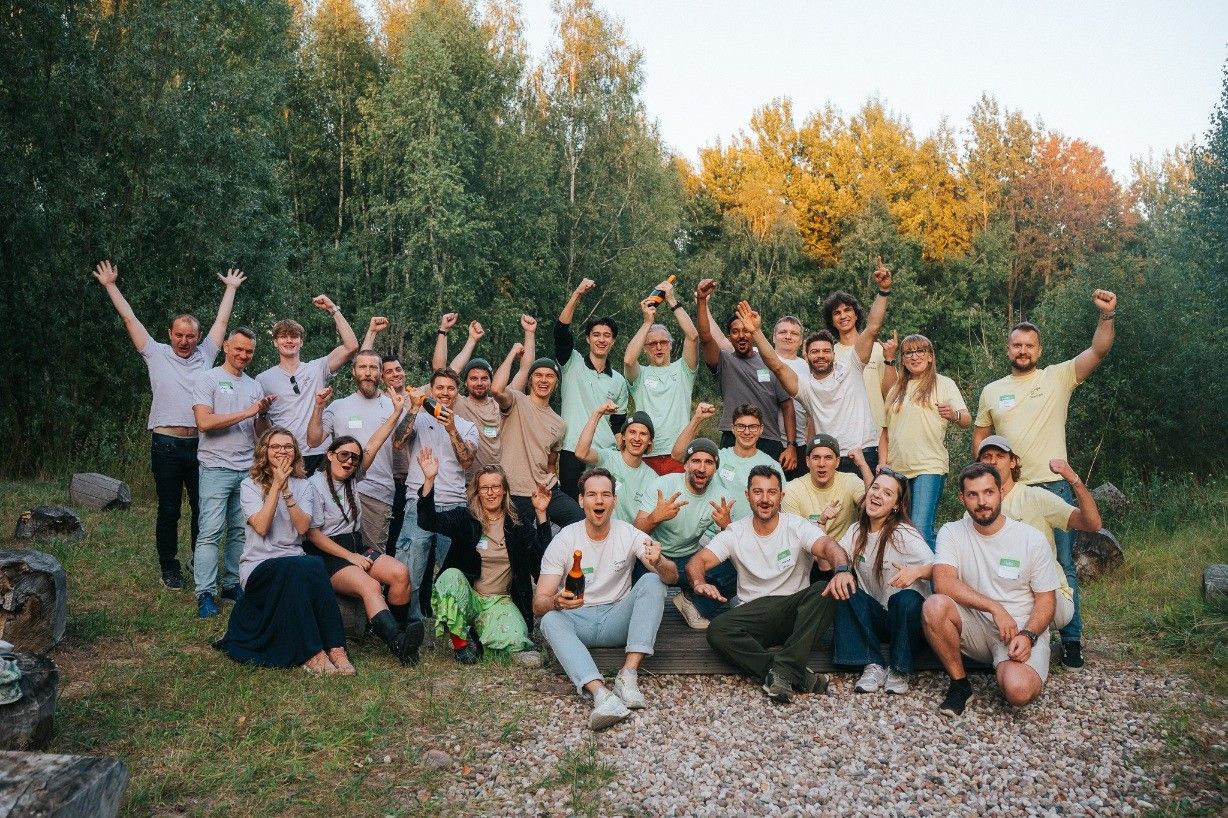 Group photo of about thirty founders and organisers cheering outdoors by a forest.