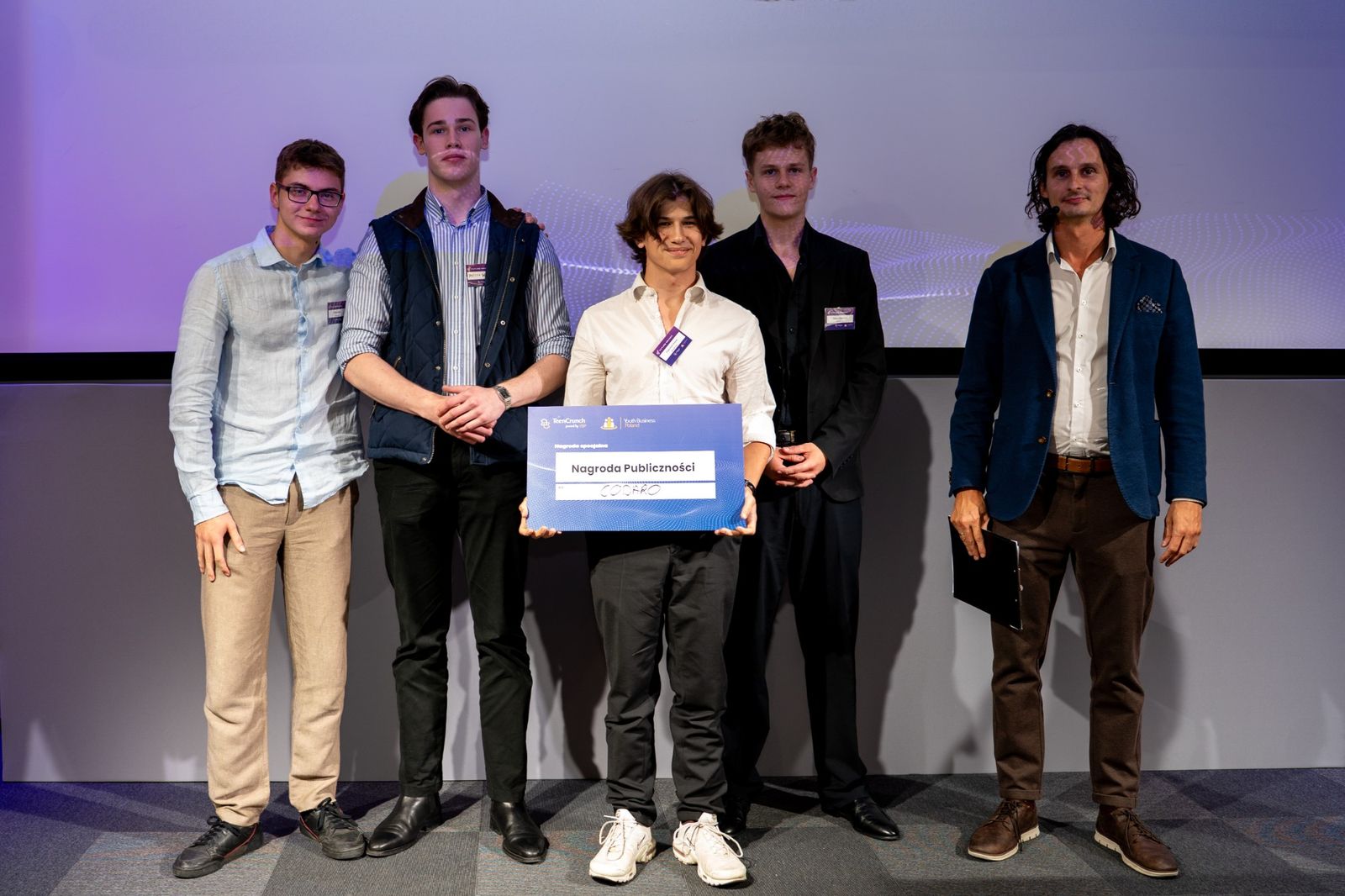 Four members of the Codaro team on stage holding a TeenCrunch Audience Award board, next to the host.