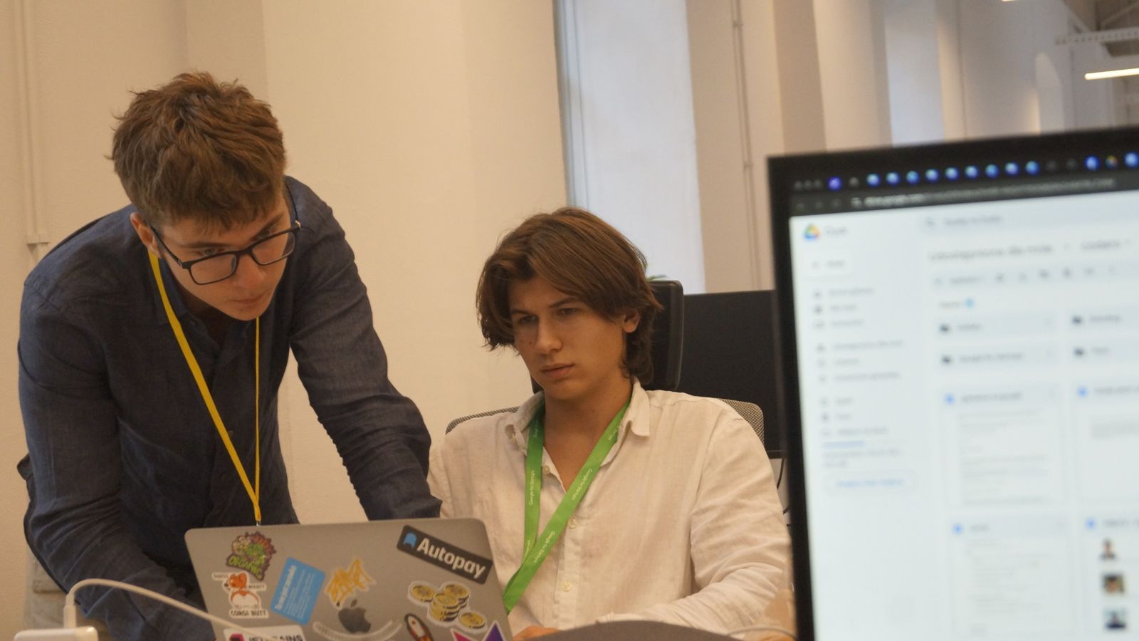Mikita leaning over a teammate's laptop at the Google for Startups Campus, both wearing resident lanyards.