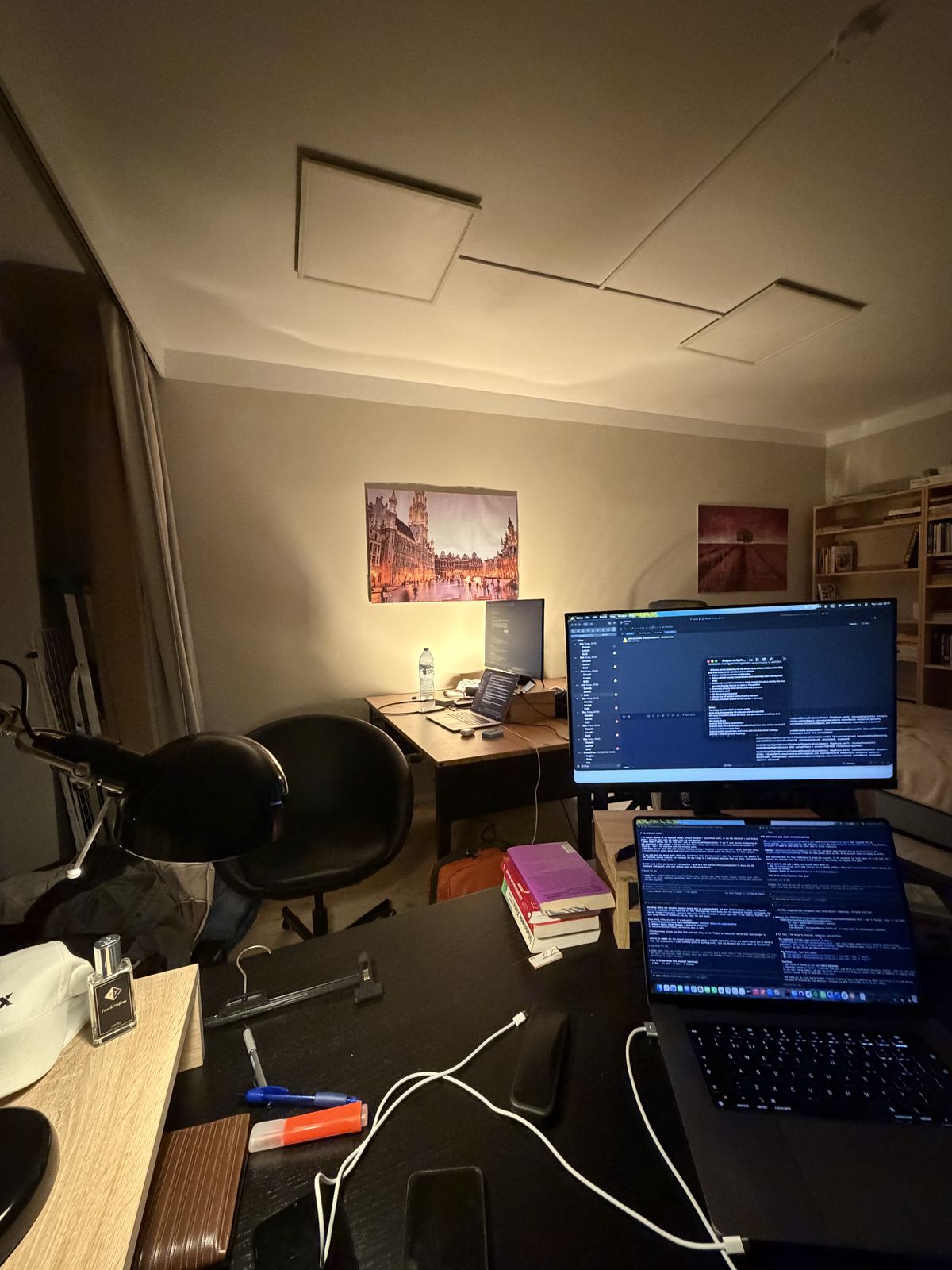 Late-night desk in the Warsaw apartment: a laptop and monitor full of code, a second desk in the background.